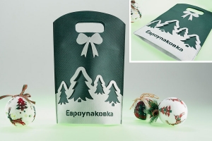 28008 - Зеленая промо сумка шоппер из спанбонда с вырубными ручками, по сторонам суки пришит фигура банта и фигурная вырезная вставка из белого спанбонда образующие обьемный рисунок, на самой белой вставке имеются фигурные вырезы фоном для которых является основной материал сумки.